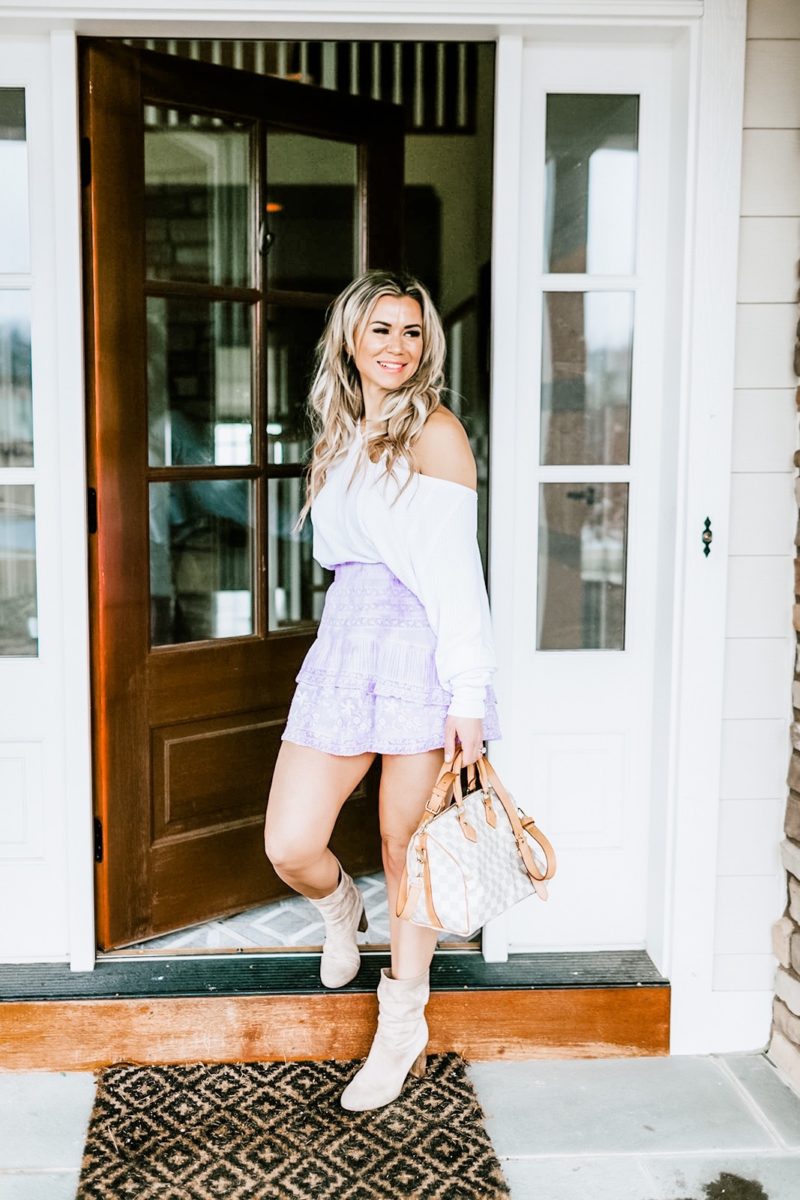 Kelly Ruth wearing a stylish outfit provided by Nuuly. Outfit includes a tiered purple skirt, white top, suede ankle boots and a Louis Vuitton purse.